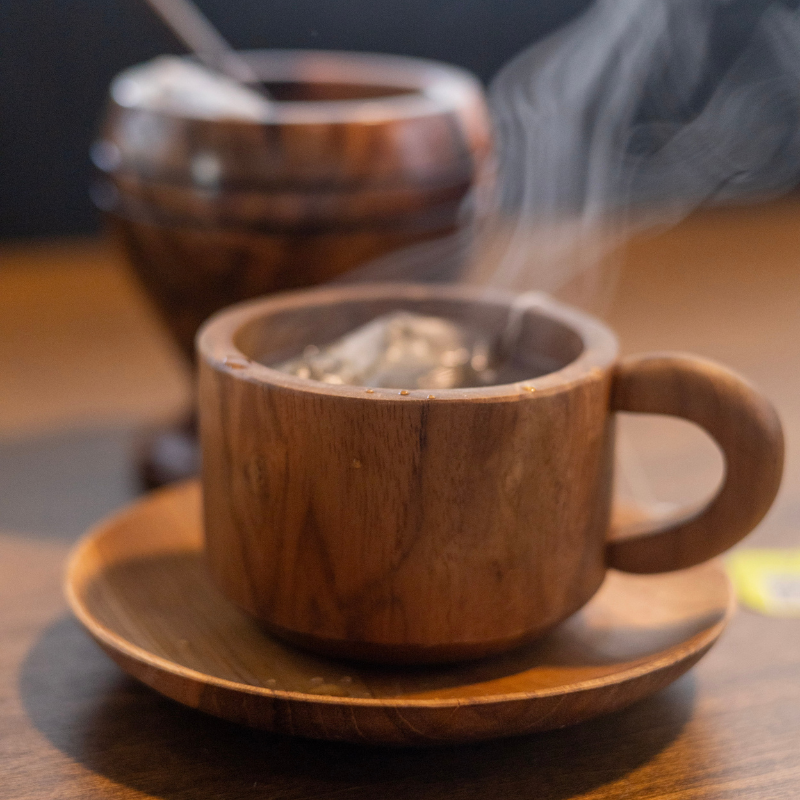 Handcrafted teak wood cup and saucer set with a steaming hot beverage, showcasing its natural grain and rustic elegance. Perfect for enjoying tea, coffee, or any warm drink in style.