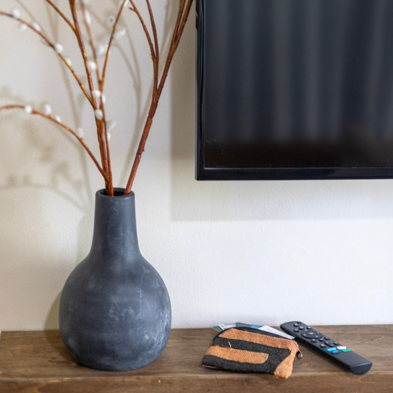 Handwoven natural fiber pouch in black and earthy orange tones, placed on a wooden table alongside a remote and decorative vase, showcasing its versatility and compact design for everyday use.