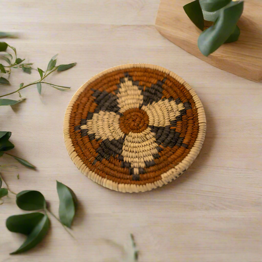 Handwoven natural fiber trivet featuring an earthy geometric pattern in black, tan, and cream tones. Perfect for protecting surfaces while adding artisan charm to your kitchen or dining area.