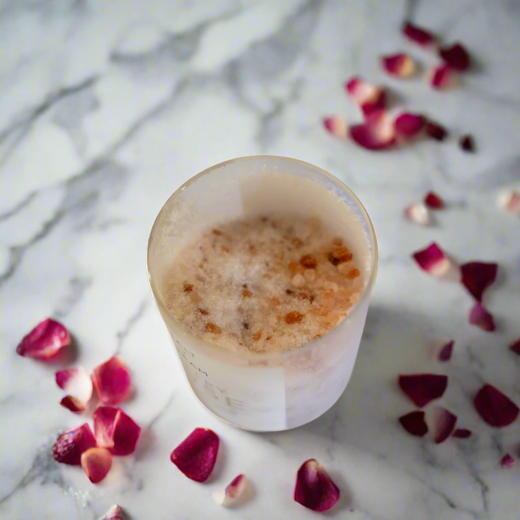 The image shows a jar of Salt + Steam Sultry Rose Bath Salts, elegantly styled with a cork lid. The jar rests on a bed of pink and white bath salts scattered across a smooth marble surface. The minimalist label highlights the product name and details, featuring "Rose & Black Pepper Luxury Bath Salts" with a net weight of 432g. This arrangement emphasizes a luxurious, natural, and soothing aesthetic, perfect for self-care and relaxation.