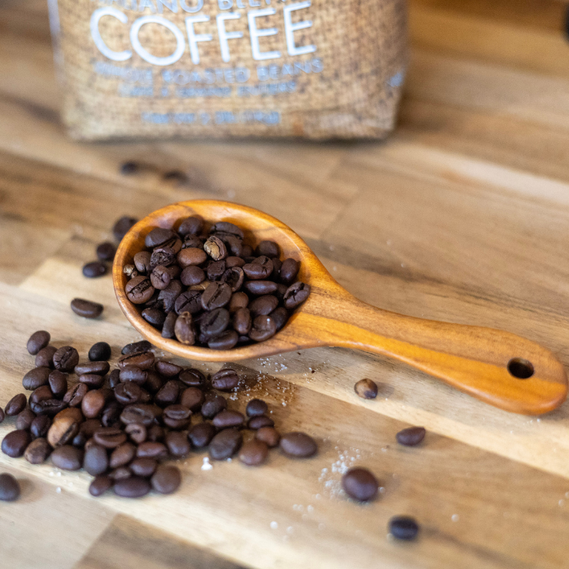 Handcrafted hardwood coffee scoop filled with dark roasted coffee beans, resting on a natural wooden countertop with a burlap coffee bag in the background, evoking a warm and rustic coffeehouse vibe.