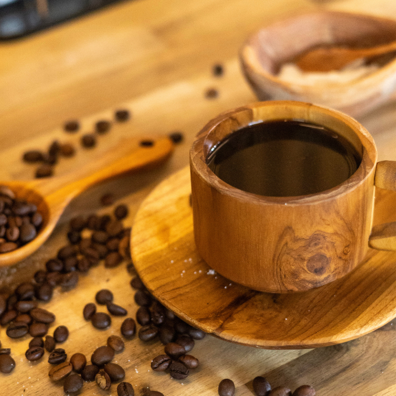 Handcrafted teak wood cup and saucer set, filled with coffee, displayed on a rustic wooden surface surrounded by coffee beans, showcasing its natural elegance and artisanal design.