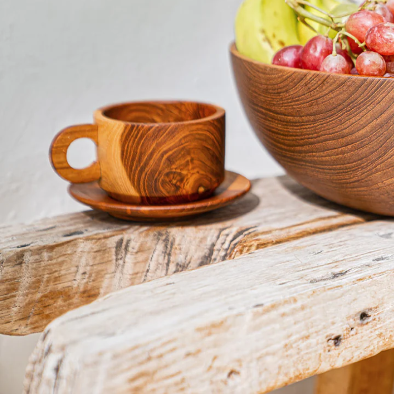 Handcrafted teak wood cup and saucer set with a rich natural grain, displayed on a rustic wooden table beside a matching fruit bowl, highlighting its elegance and artisan craftsmanship.