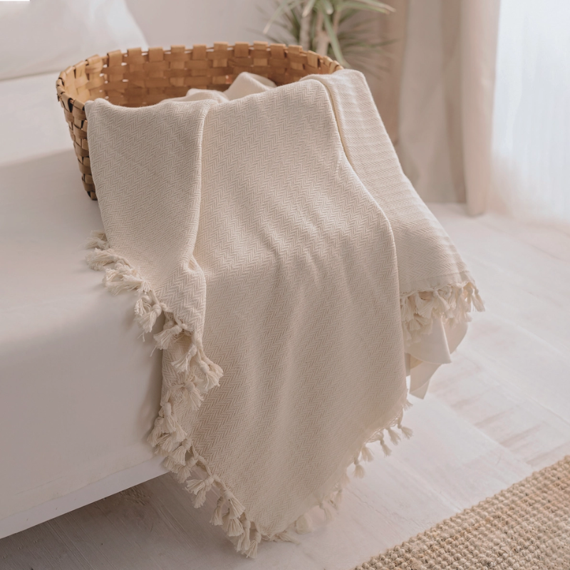 Soft cream farmhouse throw blanket with a chevron pattern and decorative tassels, styled on a bed and basket, adding warmth and rustic charm to any space.